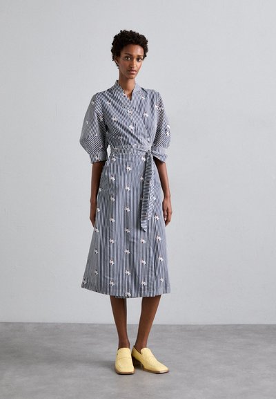 Robe en coton rayée avec des manches courtes bouffantes, dotée d'une ceinture à nouer et de petits motifs floraux. Associée à des chaussures jaunes en tressage à enfiler.