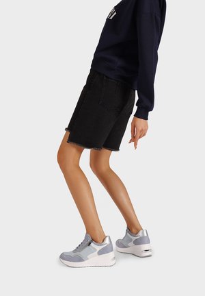 Shorts in denim nero con orlo sfrangiato, abbinati a scarpe da ginnastica grigie e azzurro chiaro con suola bianca e dettagli in argento.
