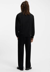 Sort ribbet sweater med lange ærmer, rund halsudskæring og matchende sorte bukser med afslappet pasform. Glat tekstur og minimalistisk design.