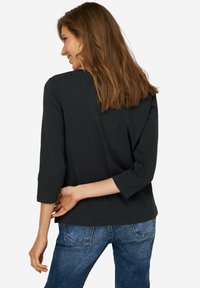 Top nero a tre quarti in tessuto liscio, con scollatura rotonda e vestibilità rilassata, abbinato a jeans in denim blu.