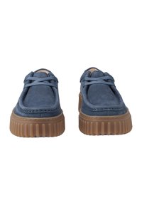 Zapatos de ante azul con puntera redonda, diseño de cordones, superficie texturizada y una suela de goma marrón gruesa y estriada.
