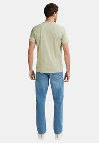 Helles grünes kurzärmliges T-Shirt aus Baumwolle, Rundhalsausschnitt, kombiniert mit hellblauen Denim-Jeans, gerader Schnitt, Fünf-Taschen-Design.