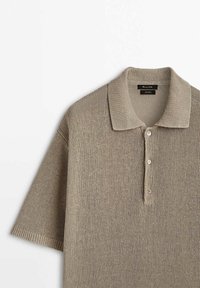 Knit polo shirt in light beige, featuring a ribbed collar, short sleeves, three button placket, and textured fabric throughout.