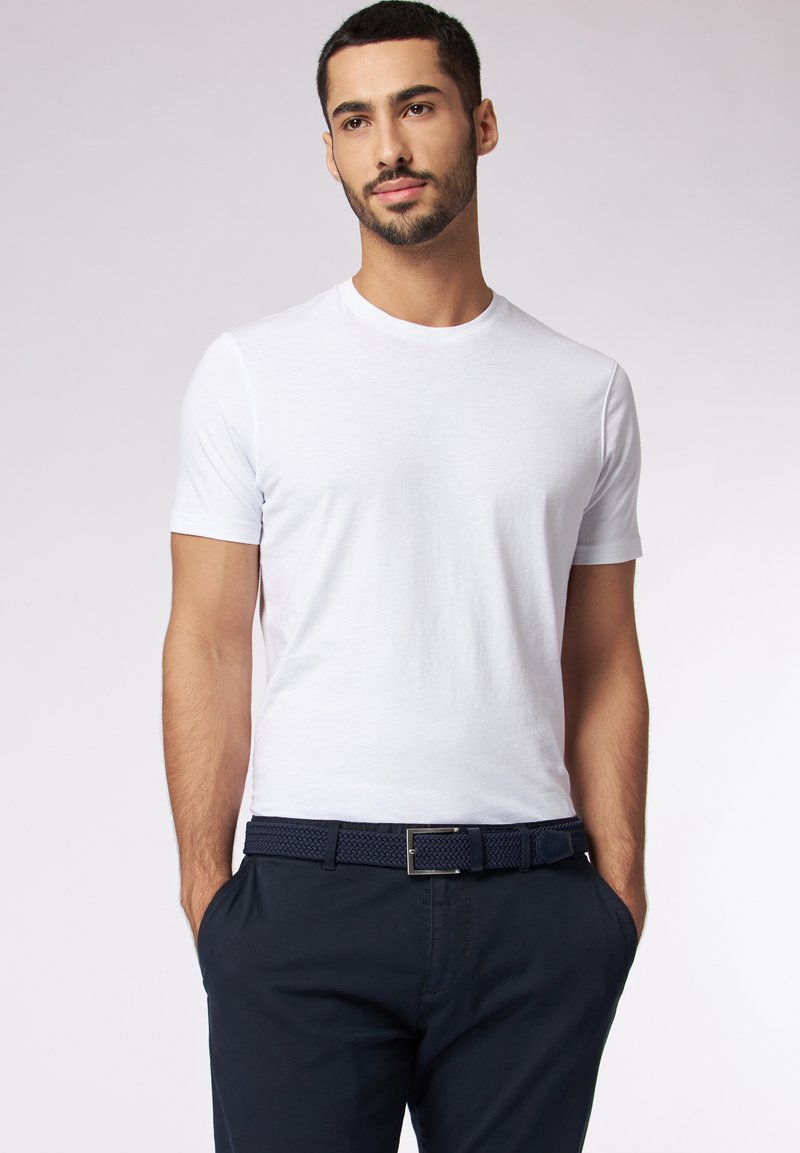 T-shirt blanc à manches courtes en tissu doux, décolleté ras du cou, porté avec une ceinture tissée marine et un pantalon sombre, avec une texture lisse.