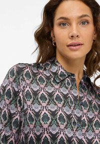 Button-up skjorte med et geometrisk print i sort, grøn og pink. Stoffet er glat og har krave samt knaplukning.