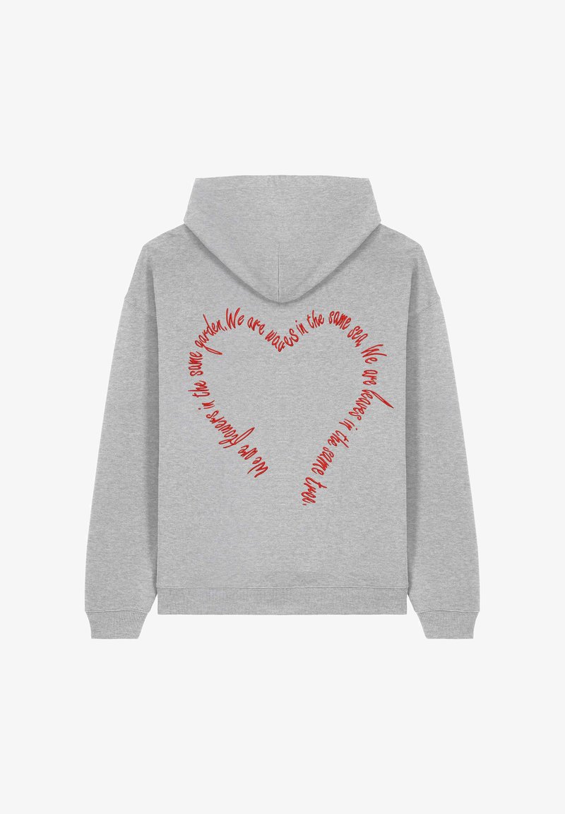 Szürke kapucnis pulóver, amelynek hátulján egy piros szív alakú szöveges dizájn található, amely a következő üzenetet tartalmazza: "Ugyanannak a tengernek a hullámai vagyunk."