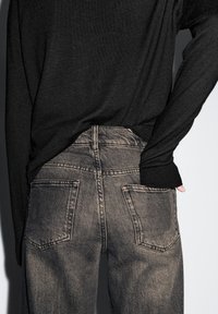 Schwarz langärmliges Oberteil kombiniert mit dunkelgrauen hoch geschnittenen Jeans. Die Jeans verfügen über zwei Gesäßtaschen und eine strukturierte Oberfläche.