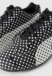 Μαύρα αθλητικά παπούτσια με λευκές πουά, μαύρα κορδόνια και λευκή πλαϊνή ρίγα με μικρότερες μαύρες πουά.