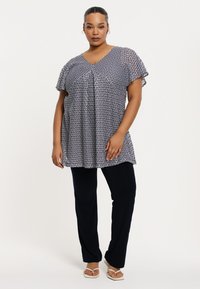 Marineblaues und weißes Tunika mit Zickzackmuster, V-Ausschnitt und kurzen Flatterärmeln, kombiniert mit schwarzen Hosen. Glatter Stofftextur.