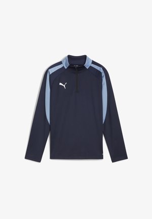 Lusikka sininen pitkähihaisen päällisen, jossa on vetoketjullinen mock-kraavu; siinä on vaaleansinisiä olkapään korostuksia ja valkoinen logo rinnassa. Sileä kangastuntuma.