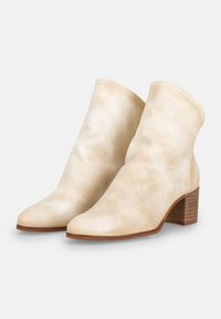 Bottines beiges en cuir texturé, avec un bout pointu et un talon en bois épais, présentant des coutures visibles sur les bords.