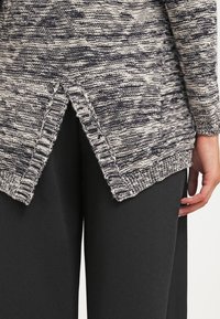 Pull en tricot dans un motif marbré gris et noir, avec un ourlet en V et des poignets côtelés. Associé à un pantalon noir pour le contraste.
