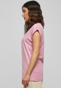 Roze T-shirt met korte mouwen van zachte katoen, met een ontspannen pasvorm en opgerolde randen. Gladde textuur met een eenvoudig ontwerp, gedragen met beige broek.