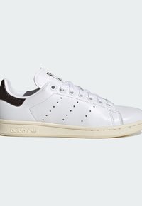 Άσπρο χαμηλό adidas sneaker με μαύρη ταμπέλα στη φτέρνα, διάτρητες πλαϊνές ρίγες, λευκά κορδόνια και εκρού λαστιχένια σόλα.