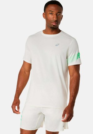 Athletischer Mann, der ein schlichtes weißes T-Shirt mit kurzen Ärmeln und passende Shorts mit grünen Akzenten trägt, vor einem schlichten weißen Hintergrund stehend.