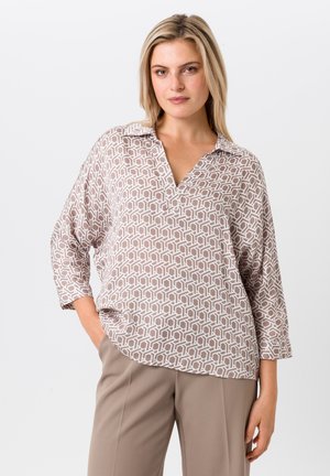 Leichte, beige Bluse mit geometrischem weißen Muster, Kragen und drei Viertelärmeln. Kombiniert mit taillierten beigefarbenen Hosen.