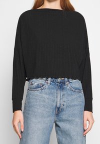 Black ribbed long-sleeve top with a cropped hem, paired with light blue high-waisted jeans. Casual and relaxed design.