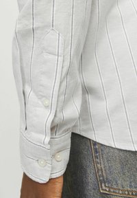 Biała koszula w paski zapinana na guziki, z szarymi pionowymi liniami, posiadająca mankiety z dwoma perłowymi guzikami i teksturowanym wykończeniem materiału.