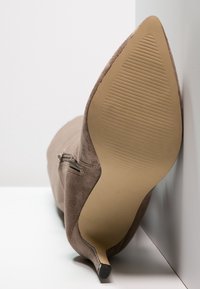 Zapato de tacón alto de ante marrón con punta afilada y suela texturizada. Cuenta con una cremallera lateral y un diseño elegante de tacón.