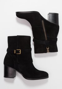 Botas de tobillo de ante negro con tacón cuadrado, detalle de hebilla dorada y cierre lateral con cremallera. Textura suave y diseño estructurado.
