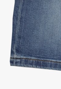 Denim-kangas keskisinisessä sävyssä, jossa on kontrastiväri ruskea sauma helmassa. Sujuva tekstuuri, jossa on hieman venyvyyttä.