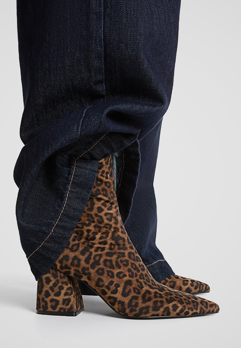 Bottes cheville à motif léopard avec un bout pointu, fabriquées en tissu doux, dotées d'un talon bloc et portées avec un jean denim foncé retroussé.