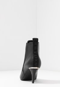 Svarta läderankleboots med en texturerad elastisk sidopanel, smal klack och en märkesdragflik baktill. Silverfärgad klackaccent.
