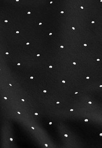 Tissu noir à texture lisse, présentant un motif de petits points blancs uniformément espacés sur toute la surface.