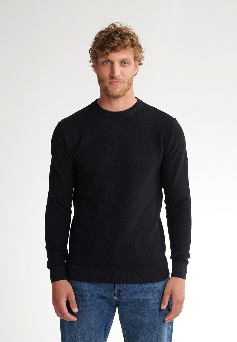 Black, textured crewneck sweater with long sleeves. Ribbed cuffs and hem. Worn with blue denim jeans. No visible logos or patterns.