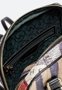 Offener, mehrfarbiger Rucksack mit einem dunkelgrünen Stoffinnenteil, schwarzem Reißverschlusstaschen und goldenen Reißverschlussanhänger.