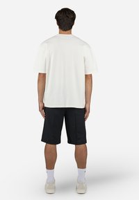 Tricou alb din bumbac, cu mâneci scurte și o croială lejeră, asortat cu pantaloni scurți negri. Design simplu, fără logo-uri sau modele vizibile.