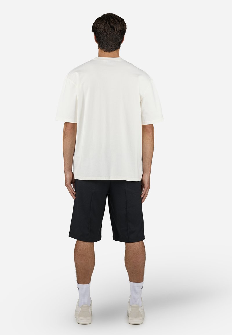 Weißes Baumwoll-T-Shirt mit kurzen Ärmeln und lässiger Passform, kombiniert mit schwarzen Shorts. Einfaches Design, keine sichtbaren Logos oder Muster.