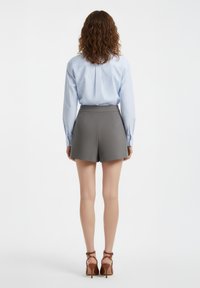 Pantaloncini grigi su misura a vita alta, con tasche laterali e texture liscia, abbinati a una camicia a righe azzurra a maniche lunghe.