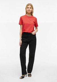 Rød kortærmet t-shirt parret med højttaljede sorte bukser og sorte sandaler med åbne tæer. Glat stof med en afslappet pasform og lige ben.