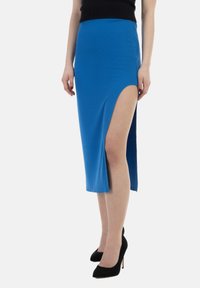 Gonna midi blu in tessuto a coste, con uno spacco alto su un lato. Combinata con scarpe nere con tacco alto.