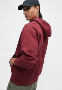 Sweatshirt com capuz de cor borgonha, feito de um tecido misto de algodão, com um bolso frontal, punhos canelados e um corte descontraído.