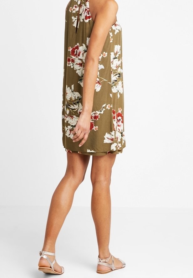 Robe sans manches à fleurs en vert olive avec des fleurs blanches et rouges ; coupe décontractée, longueur au-dessus du genou, associée à des sandales argentées.