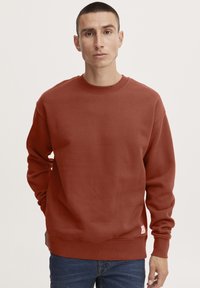 Roodbruine sweatshirt met een ronde hals, lange mouwen en geribde boorden. Bevat een klein geborduurd label op de linkeronderkant.