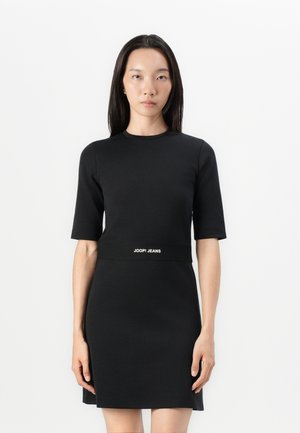 Zwarte getailleerde jurk met korte mouwen en hoge halslijn. Beschikt over een logo band op de taille en een gladde, gestructureerde stof.