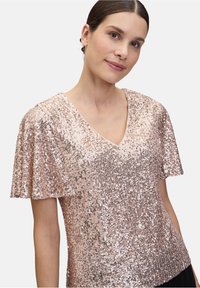Top rosa con paillettes, scollo a V e maniche corte a drappo, caratterizzato da una texture liscia e una superficie scintillante e riflettente.