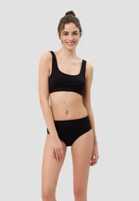 Schwarze Baumwoll-Bralette mit breiten Trägern und einem quadratischen Ausschnitt, kombiniert mit passenden hochgeschnittenen Slips. Glatte Textur, minimalistisches Design.