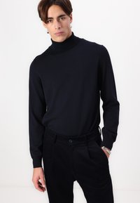 Black turtleneck sweater made of smooth knit fabric, featuring long sleeves and a fitted design, paired with dark corduroy pants.