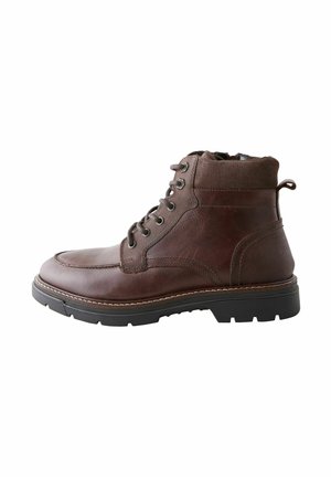 Bota de tobillo de cuero marrón con un upper texturizado, suela de goma negra, puntera redonda, seis ojales y un lazo en la parte posterior para facilitar su colocación.
