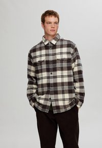 Plaid flannel shirt in cream and brown with two chest pockets, button closure, and a collared neckline, featuring a soft texture.
