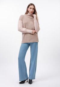 Beige coltrui met geribbelde textuur, lange mouwen, gecombineerd met lichtblauwe wijde jeans en zwarte puntige hakken.