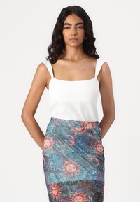 Witte tanktop met vierkante halslijn, gecombineerd met een kleurrijke rok met zon- en maanpatronen op een blauwe en teal achtergrond.