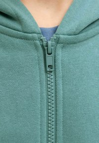 Groene hoodie met ritssluiting, uitgevoerd in een gestructureerde stof, met een ritssluiting over de volle lengte en een verstelbare capuchon met een contrasterende binnenlaag voor extra detail.