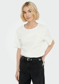 Hvid kortærmet t-shirt med rund halsudskæring, parret med højtaljede sorte jeans og et sort bælte med metalliske accenter.