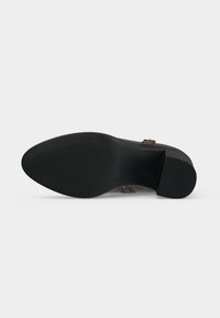 Semelle d'une chaussure en cuir brun foncé avec un petit talon carré et de fines rainures horizontales à l'avant et au talon.