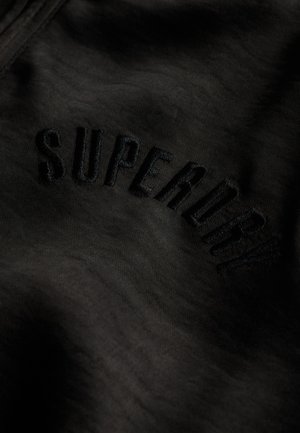Zwarte stof met geborduurde "SUPERDRY"-tekst in een bijpassende zwarte kleur, met een gladde textuur en subtiele glans.